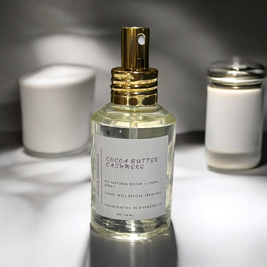 Bottle of 'Cocoa Butter Cashmere' room spray with gold nozzle on a reflective surface.